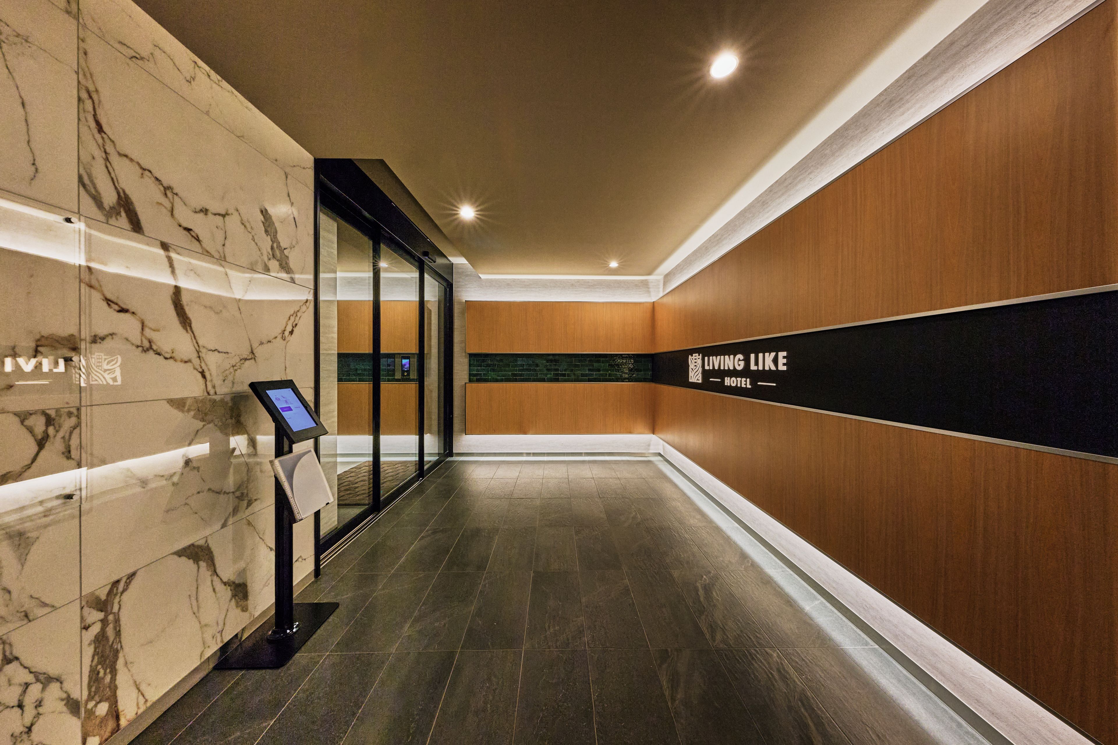 A hotel corridor with marble walls, a wooden accent wall, and a sign reading 'LIVING LIKE HOTEL'.