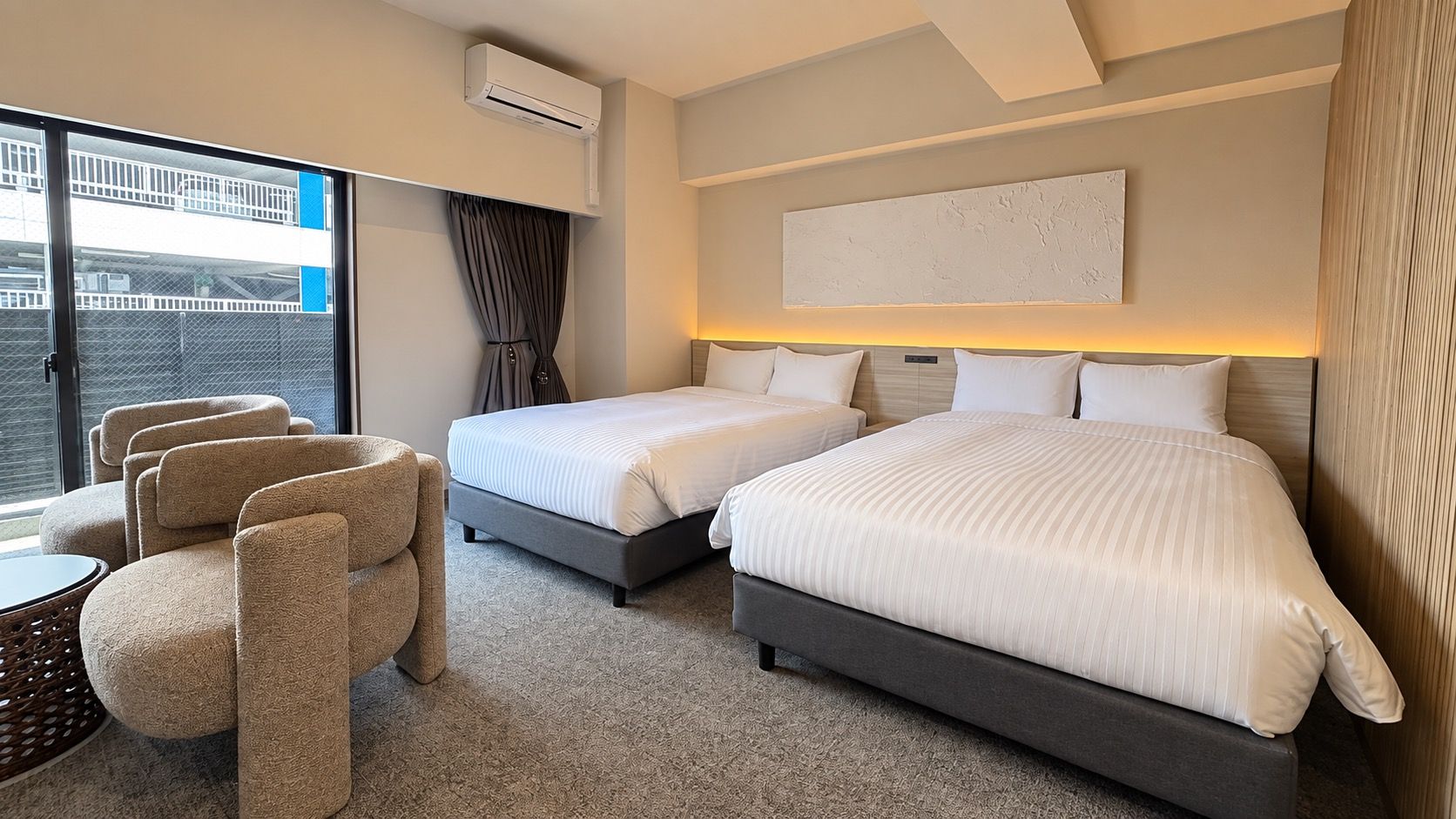 Habitación de hotel con dos camas, un sofá, una mesita y vista al exterior.