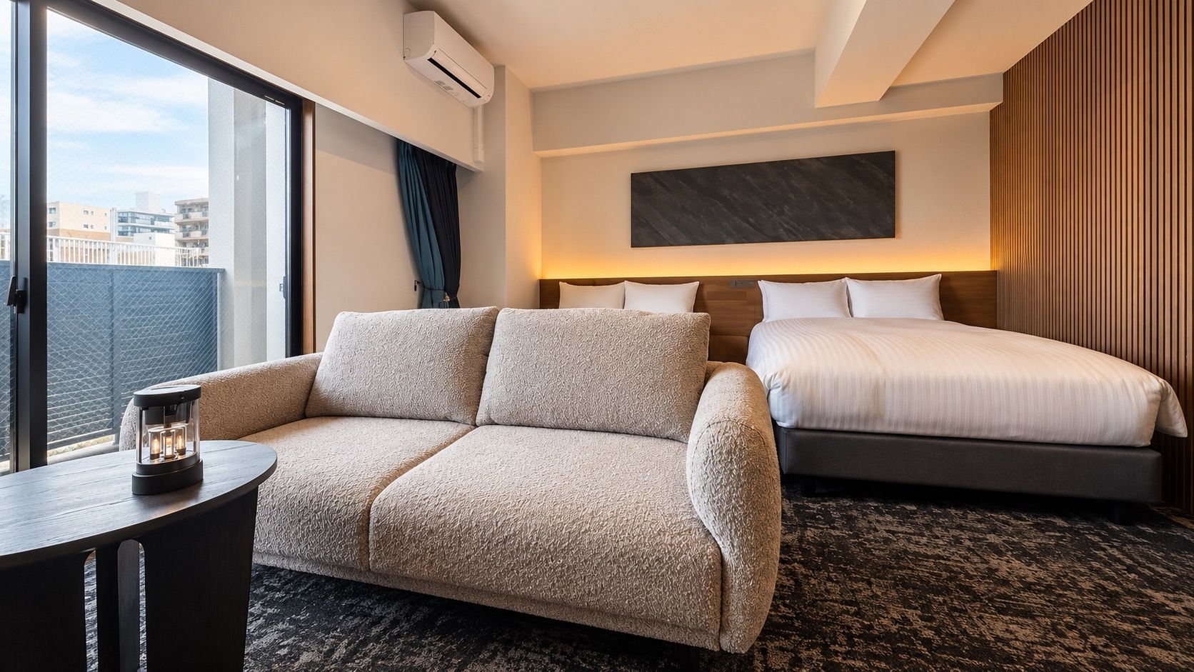 Habitación de hotel con sofá, cama, mesita de noche y vista a la ciudad.
