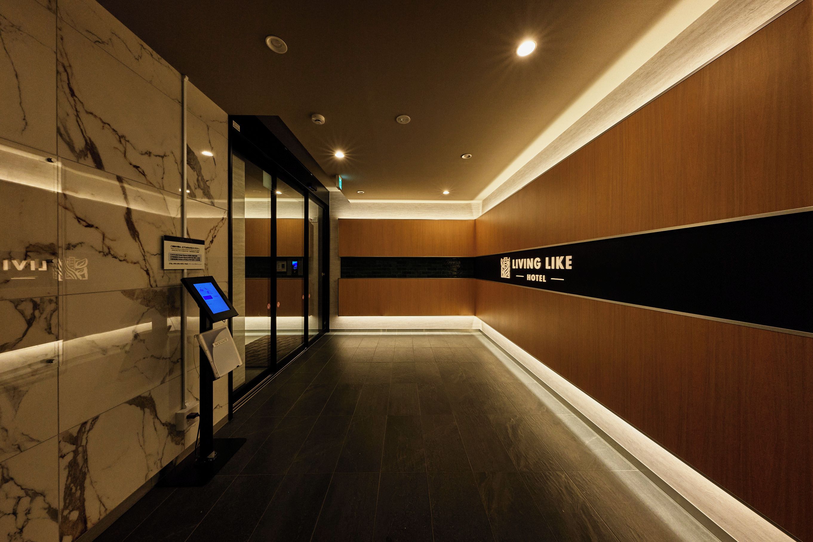 A hotel corridor with marble walls, a digital kiosk, and a sign reading 'LIVING LIKE HOTEL'.