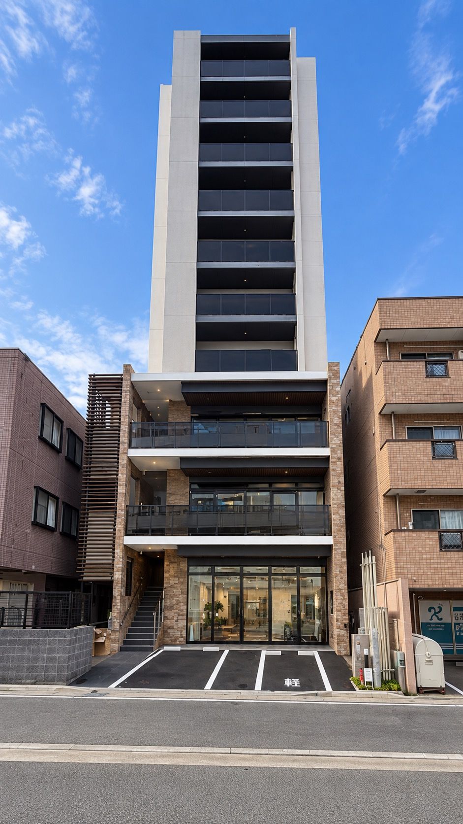 Un edificio moderno con entrada central, varios pisos y un estacionamiento al frente.