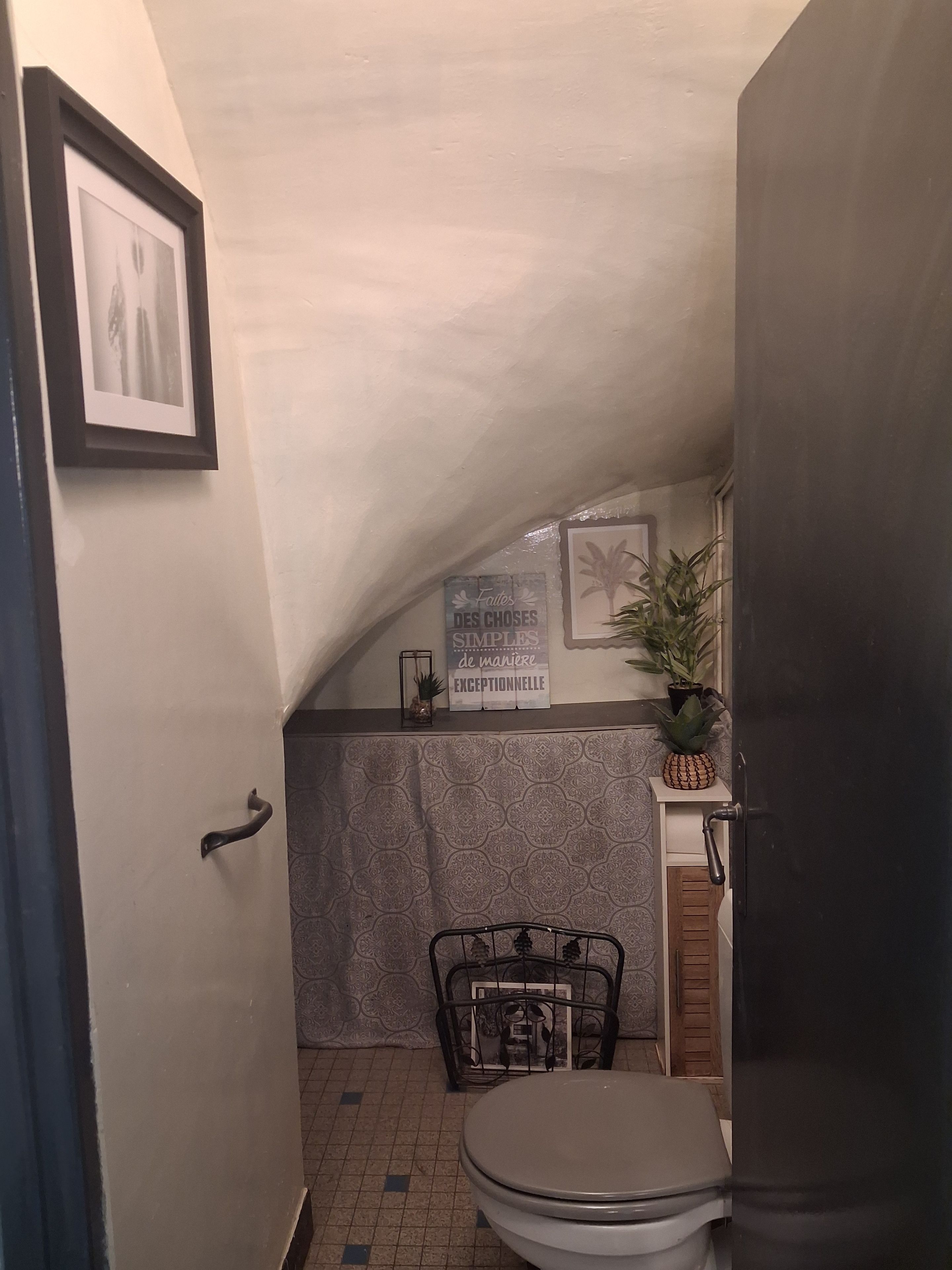 Un baño pequeño y funcional con inodoro, lavamanos y zona de ducha. Se observa un cuadro en la pared y una señal decorativa sobre el lavamanos.