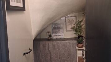 Un baño pequeño y funcional con inodoro, lavamanos y zona de ducha. Se observa un cuadro en la pared y una señal decorativa sobre el lavamanos.