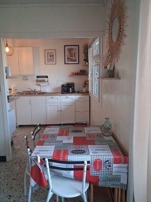 A compact kitchen with white cabinets, a coffee maker, and a dining area with a table set for two. - Vrbo Property (Millau)