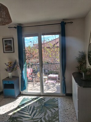 Een kamer met een schuifglasdeur die uitkomt op een buitenruimte met een terras en uitzicht op een gebouw.
