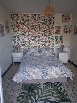 A bedroom with a bed, two bedside tables, a hanging lamp, a radiator, and a floral-patterned wall. - Vrbo Property (Millau)