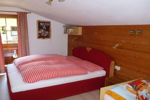 Une chambre à coucher avec une tête de lit en bois, un lit avec une literie rouge, une petite table de chevet et une étagère fixée au mur.