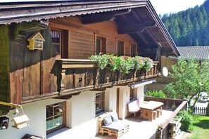 Un chalet en bois doté d’un balcon, d’un espace extérieur aménagé et offrant une vue sur la forêt environnante.