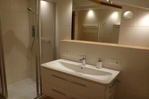 Une salle de bain avec une douche à parois de verre, un lavabo blanc avec un miroir au-dessus, et des carreaux de couleur beige.