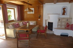 Une pièce chaleureuse avec un plafond en bois, une cheminée, un coin salon avec une table et des chaises, et une fenêtre avec des rideaux.