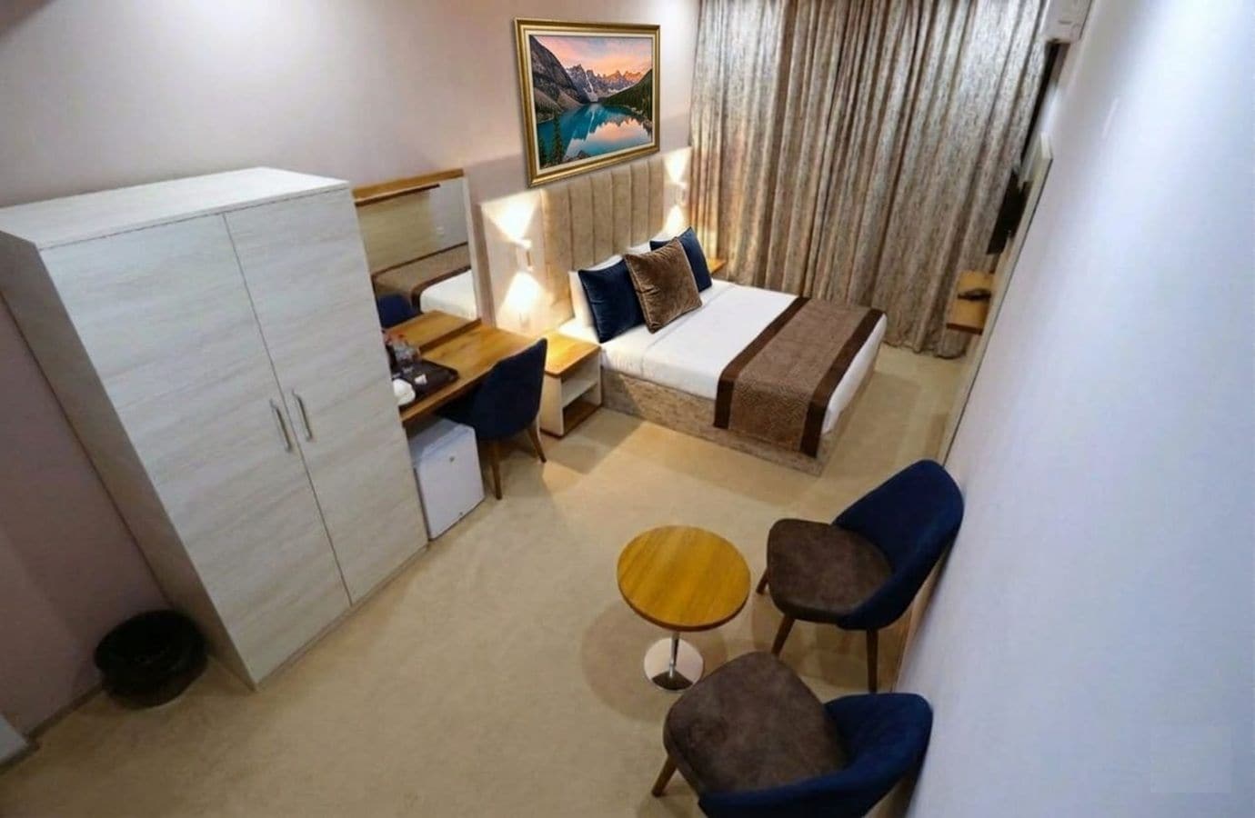 Una habitación de hotel con cama, escritorio, armario, una mesita y dos sillas.