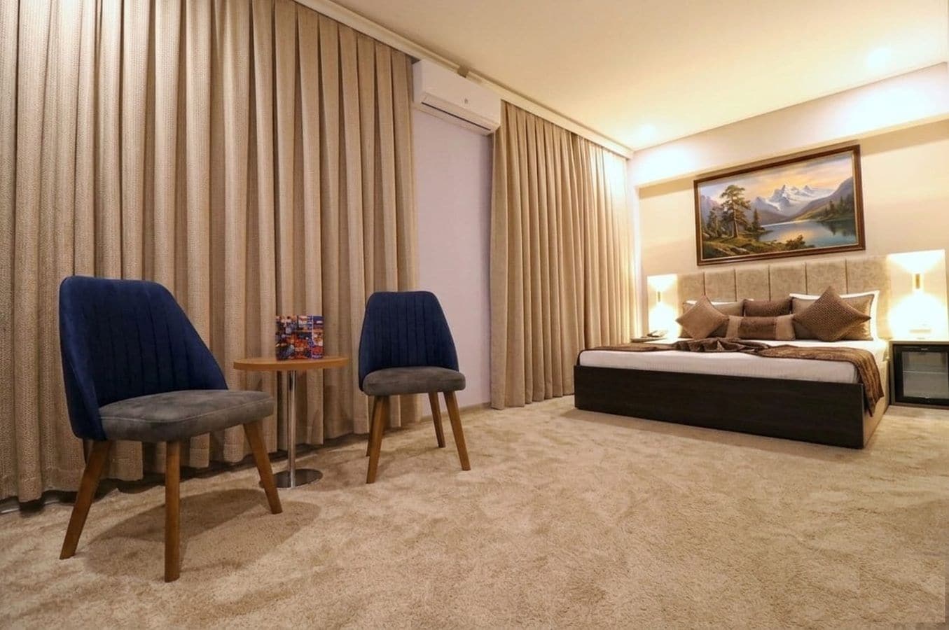 Une chambre d’hôtel avec un lit, deux chaises, une petite table et un tableau au mur.