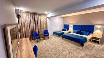 A bedroom with two beds, a desk, chairs, and a large window with curtains.