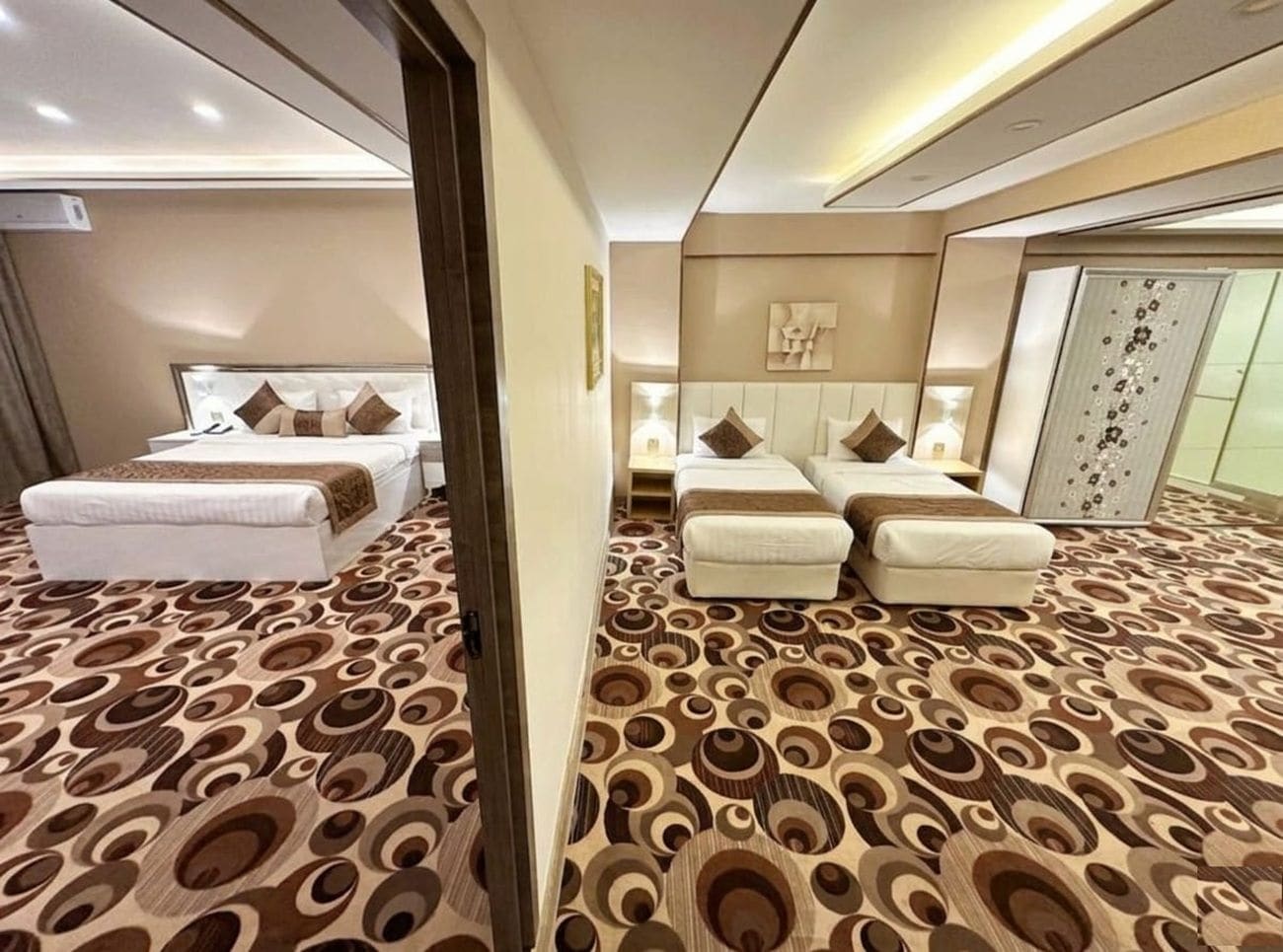 Habitación de hotel con alfombra estampada, cama con almohadas, sofá y mesita de noche.