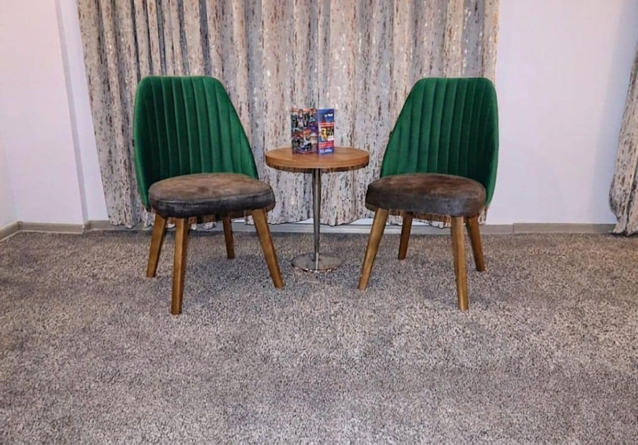 Deux chaises en bois recouvertes d’un tissu vert, ainsi qu’une petite table ronde sur laquelle se trouvent un livre et une boîte.