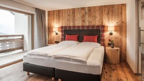 Un dormitorio con pared de paneles de madera, una cama con cabecera negra, dos lámparas de noche y una pequeña mesita de madera con un jarrón.