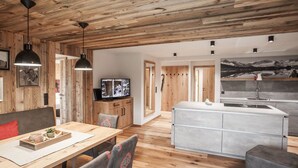 Un interior moderno con techo de madera, zona de comedor con mesa y sillas, cocina con isla central y un cuadro grande en la pared.