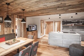 Un intérieur moderne avec un plafond en bois, un coin repas comprenant une table et des chaises, une cuisine dotée d’un îlot central et un grand tableau encadré au mur.