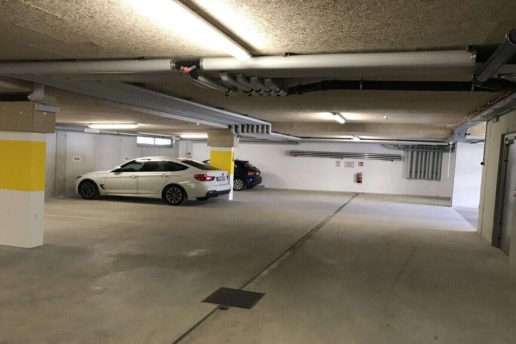 A multi-level parking garage with concrete floors and walls, equipped with overhead lighting and ventilation ducts.