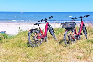 Zwei Fahrräder stehen auf einer Rasenfläche in der Nähe eines Strandes, im Hintergrund das Meer.