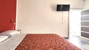 Una camera d'albergo con un letto, una televisione a parete e una porta che dà su un balcone.