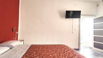 Una camera d'albergo con un letto, una televisione a parete e una porta che dà su un balcone.