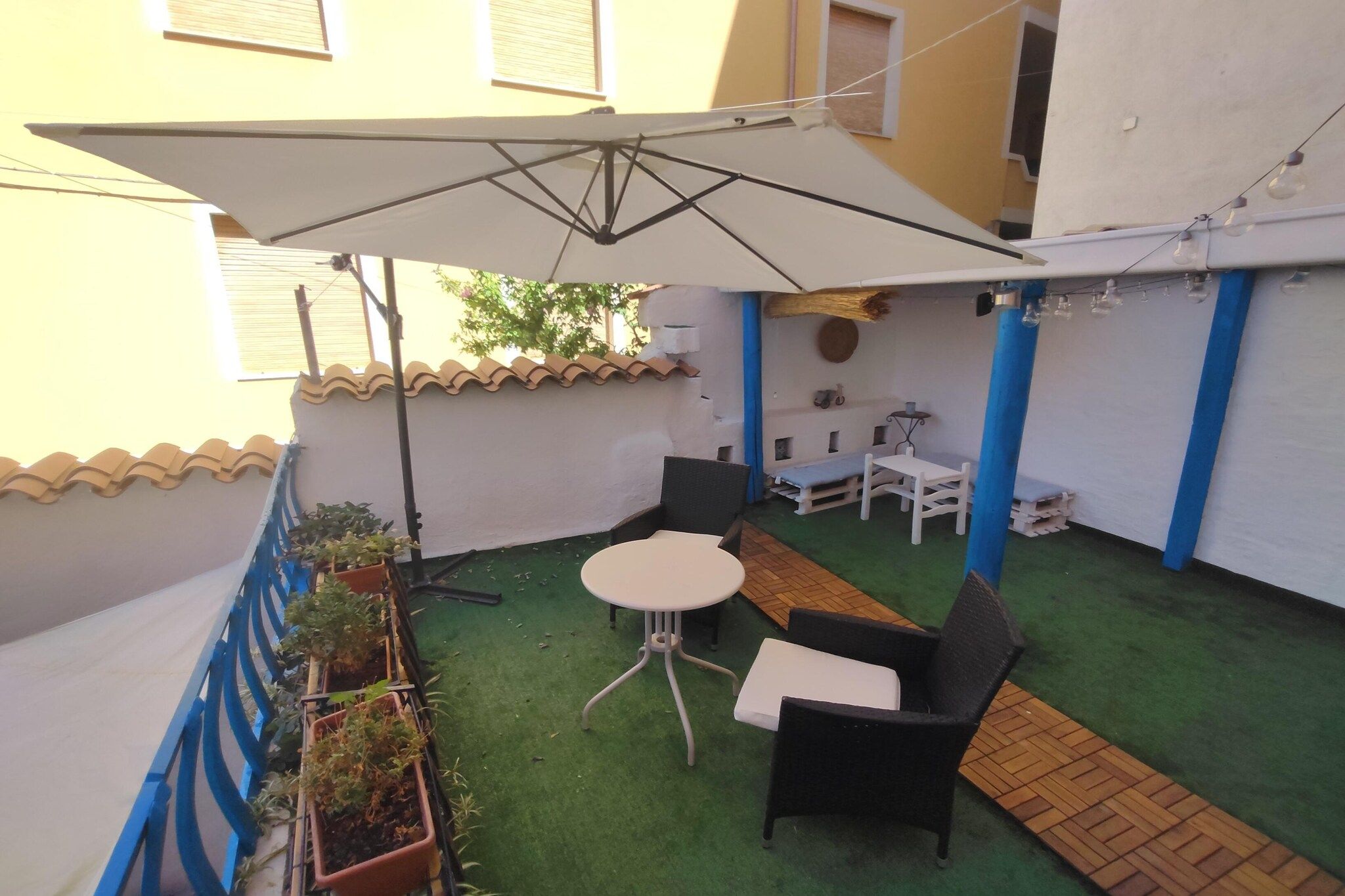 Un piccolo patio esterno con un tavolo, sedie, un ombrellone bianco e piante in vaso.