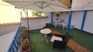Un piccolo patio esterno con un tavolo, sedie, un ombrellone bianco e piante in vaso.