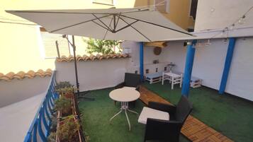 Un piccolo patio esterno con un tavolo, sedie, un ombrellone bianco e piante in vaso.