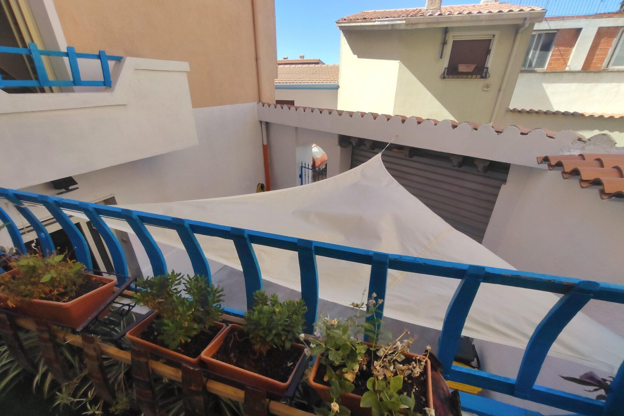 A balcony with a white awning, potted plants, and a blue railing.