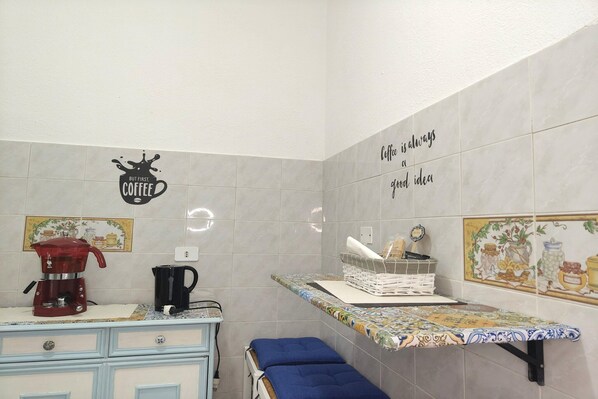 A kitchen with a coffee maker, a kettle, and a shelf with a coffee-themed sign.