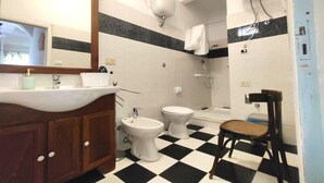 Un bagno con lavandino, due servizi igienici, bidet, specchio e pavimento a scacchi.