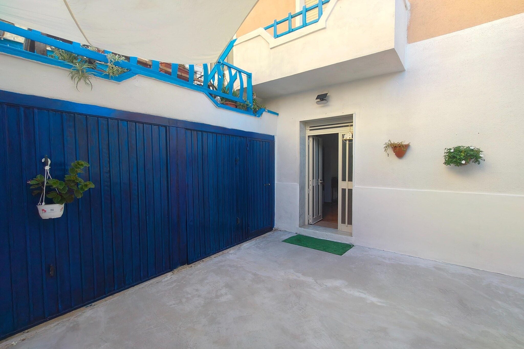 Un cancello blu, una piccola scala, una porta e una pianta in vaso.