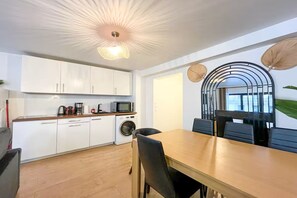 A modern kitchen with white cabinets, a microwave, and a washing machine. There is a dining area with a wooden table and black chairs. - Opera apartment in the heart of Paris (Paris)