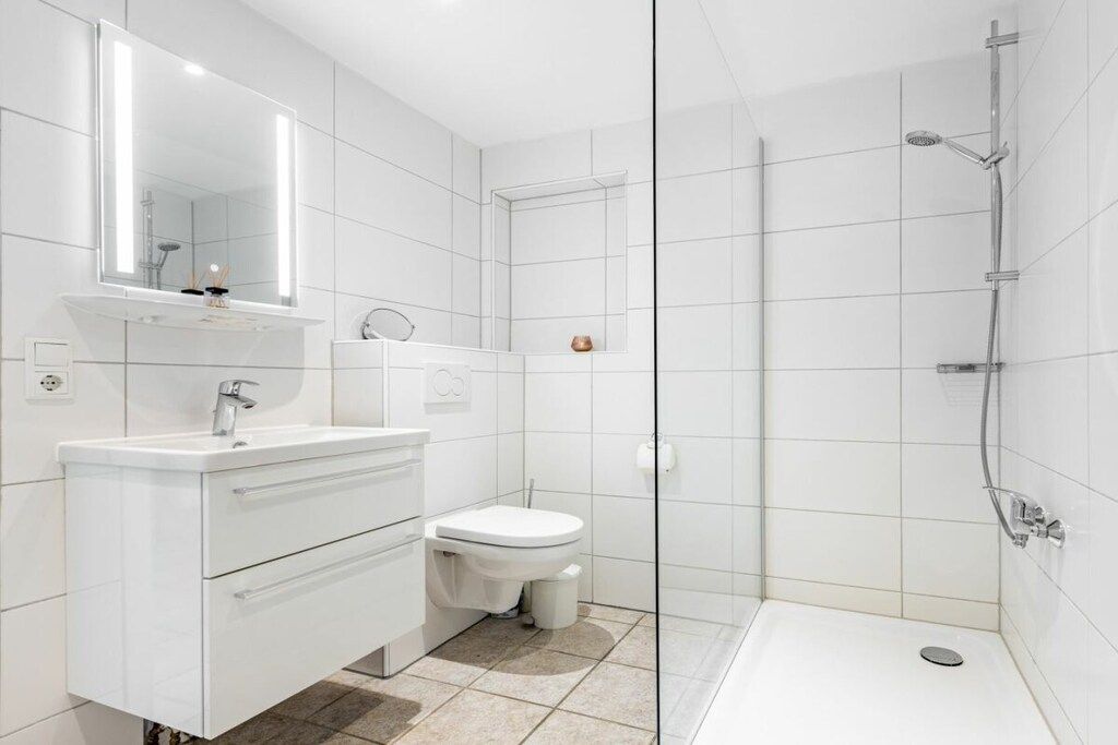 Et moderne badeværelse med et hvidt underskab, toilet, bruseniche og et stort spejl.