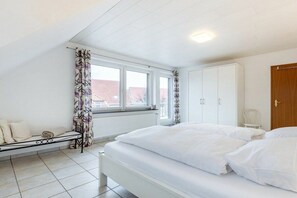Ein Schlafzimmer mit Bett, Fenster, Heizkörper, Kleiderschrank und einer Bank.
