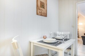 Ein Essbereich mit einem weißen Tisch, gedeckt für zwei Personen, einem gerahmten Bild an der Wand und einem weißen Stuhl.