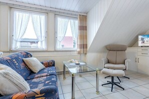 Ein Zimmer mit einer Couch, einem Glastisch, einem Sessel und einem Fernseher.