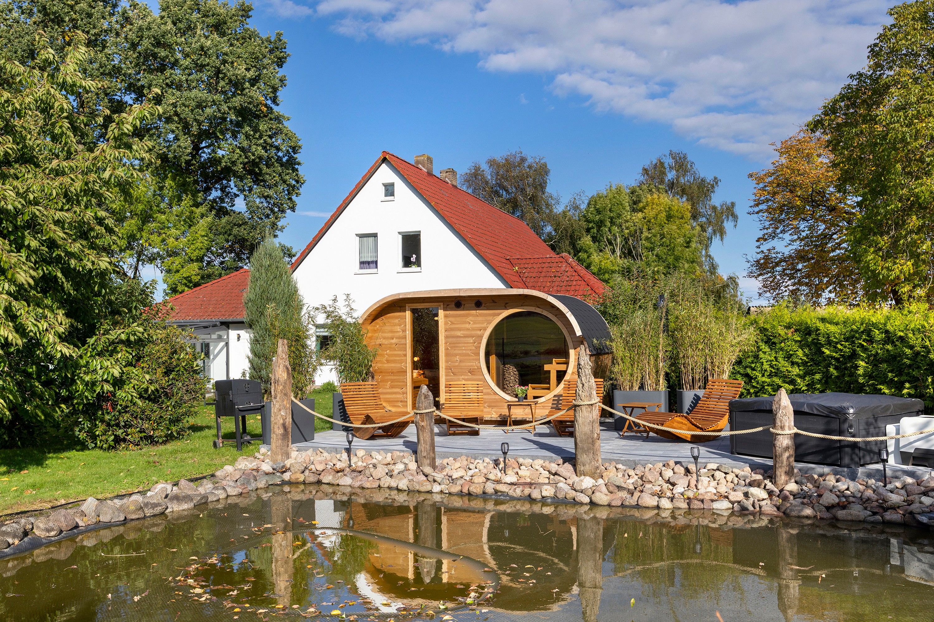 Een huis met een ronde houten uitbouw, een vijver ervoor en een rood dak.
