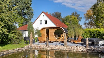 Een huis met een ronde houten uitbouw, een vijver ervoor en een rood dak.
