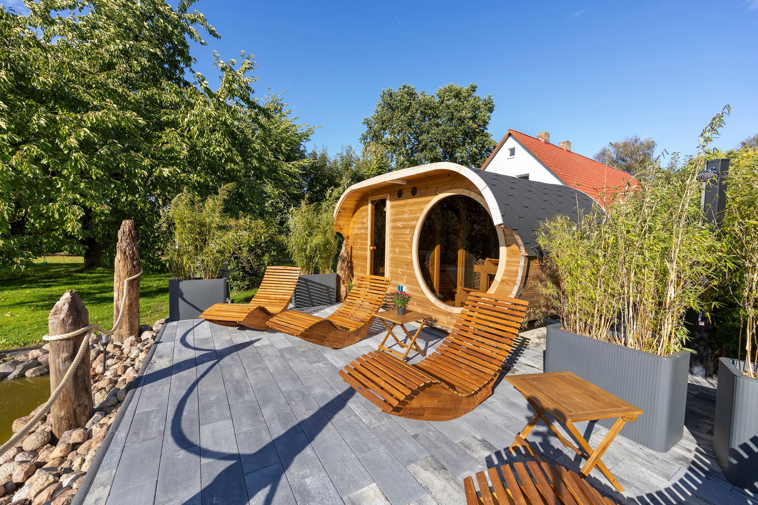 A wooden structure with a curved roof, surrounded by outdoor seating and a small water feature.