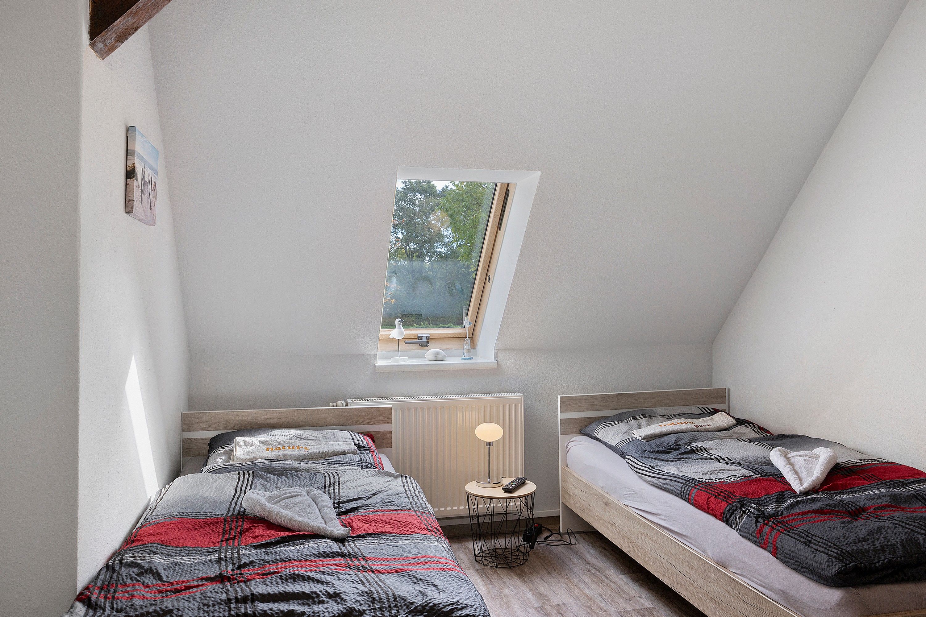 A small, well-lit room with two beds, a window, and a radiator.