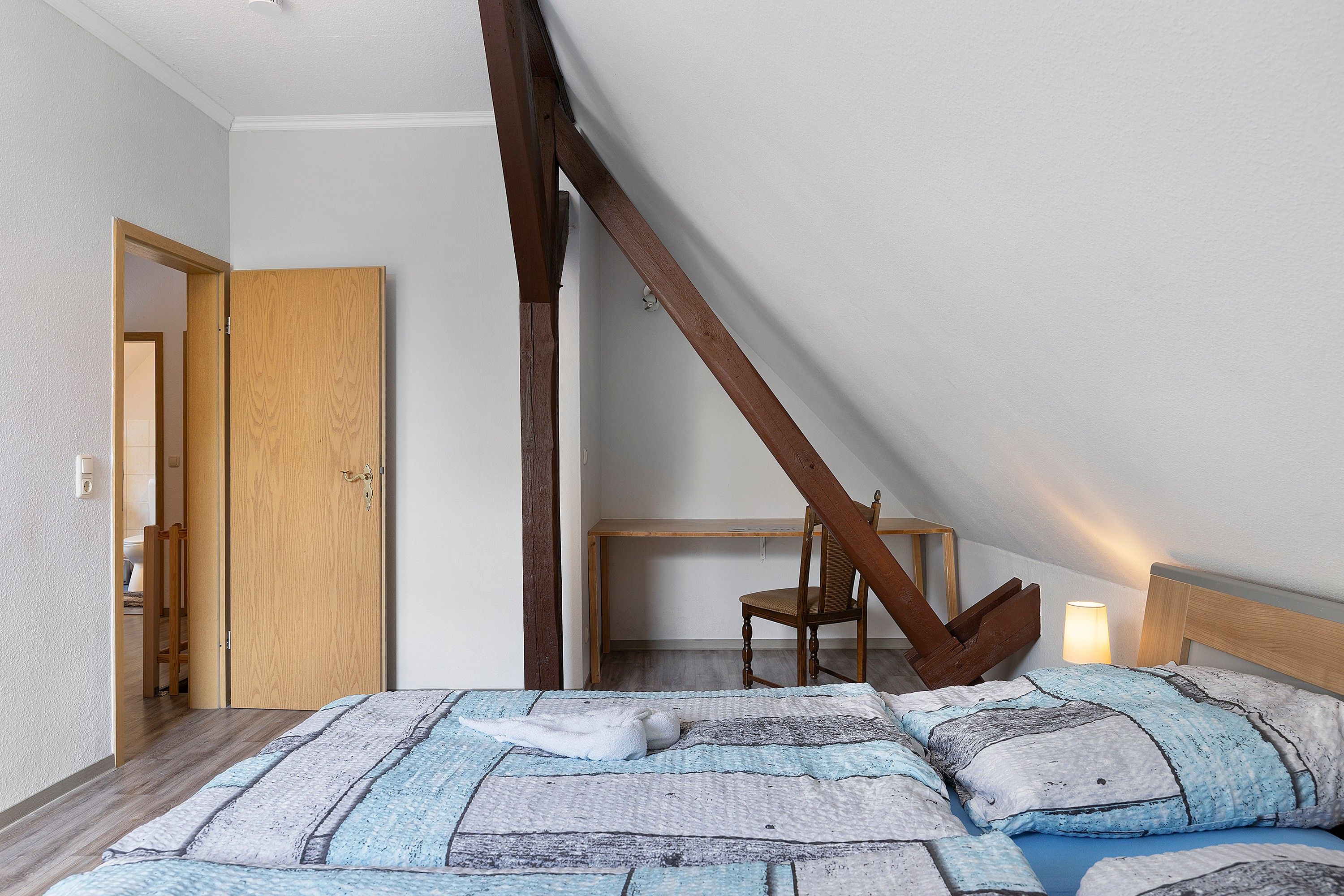 Ein Schlafzimmer mit schrägem Dach, einem Holzbettgestell, einem Nachttisch und einem Sessel.