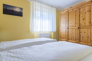 A bedroom with two beds, a window with curtains, a radiator, and wooden wardrobes. - 1 in the house "Trischen" (ID 359) (St. Peter-Ording)