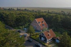 Una zona residenziale con una casa grande e un edificio più piccolo, immersa tra alberi e un cielo sereno.