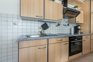 A kitchen with wooden cabinets, a stainless steel sink, a built-in oven, and a black range hood. - Holiday apartment 2 in Haus Hever (ID 048) (St. Peter-Bad)