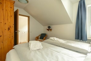 A bedroom with two single beds, a wooden wardrobe, a chair, and a small shelf with a plant. - Holiday apartment 2 in Haus Hever (ID 048) (St. Peter-Bad)