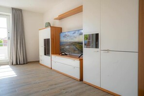 A room with a large flat-screen TV mounted on a wooden cabinet, a sliding glass door, and a light-colored floor. - Apartment 14 (ID 212) (St. Peter-Bad)