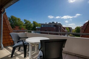 A balcony with a round table and two chairs, overlooking a residential area with brick buildings. - Apartment 14 (ID 212) (St. Peter-Bad)