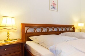 Ein Hotelzimmer mit einem hölzernen Kopfteil, zwei Betten mit weißer Bettwäsche, einem Nachttisch mit Lampe und einem Blumenbild an der Wand.